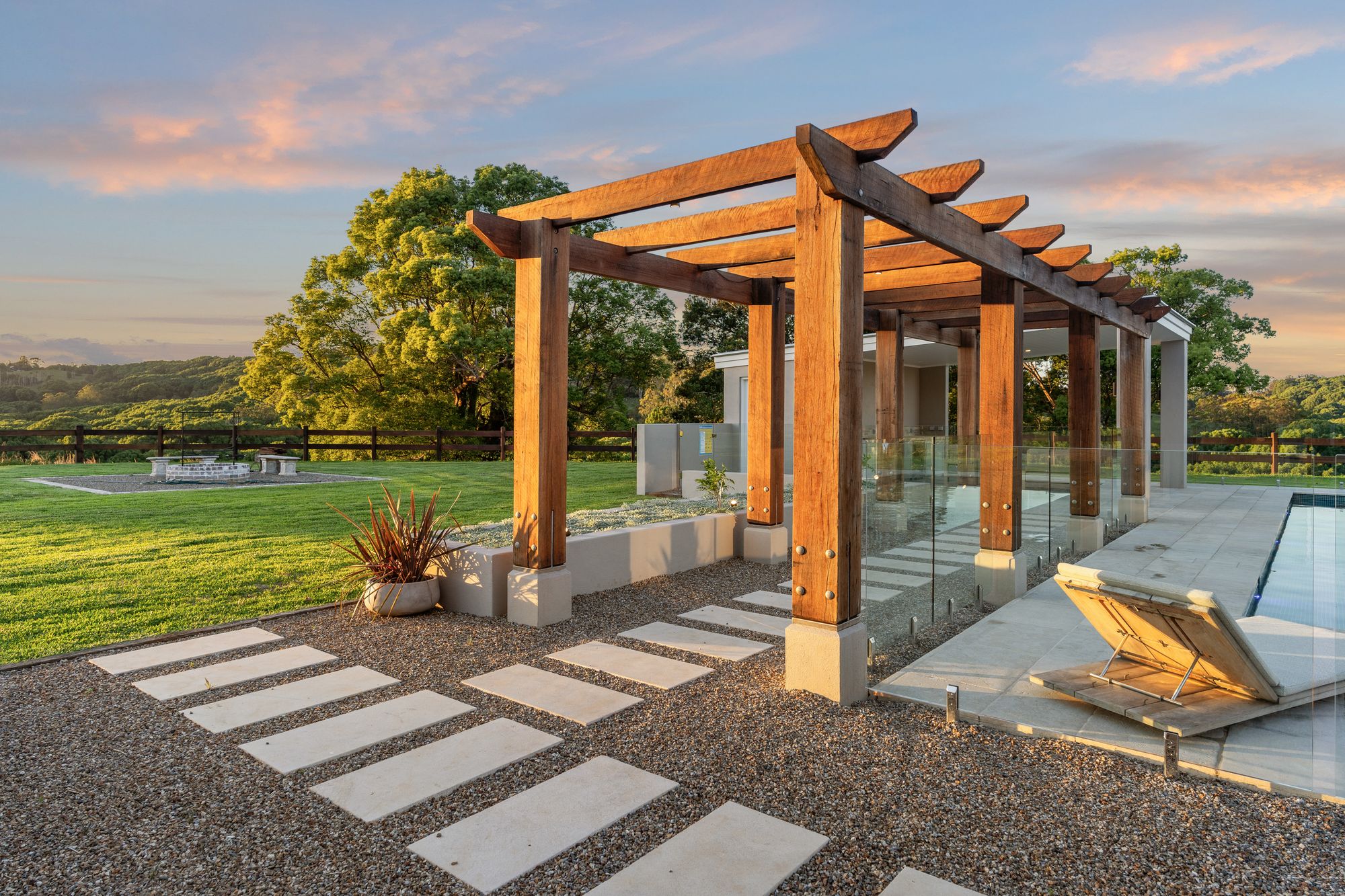 A hardwood pergola over a pool terrace at golden hour