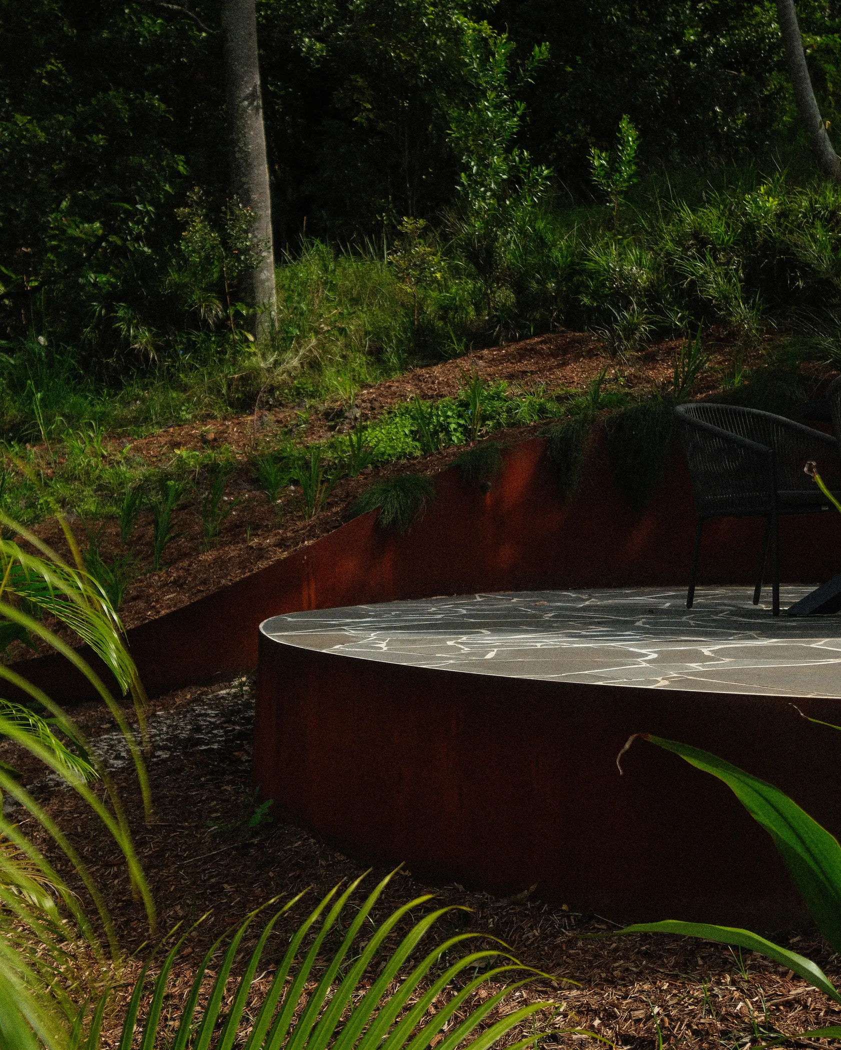A curved corten steel wall holding a crazy paved terrace on a rainforest slope