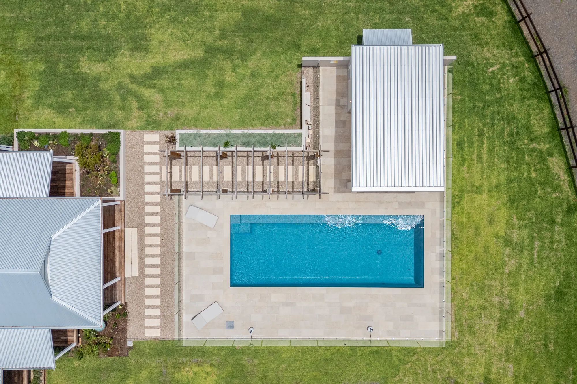 A pool, deck, lawn and paving on a rural estate seen from directly above