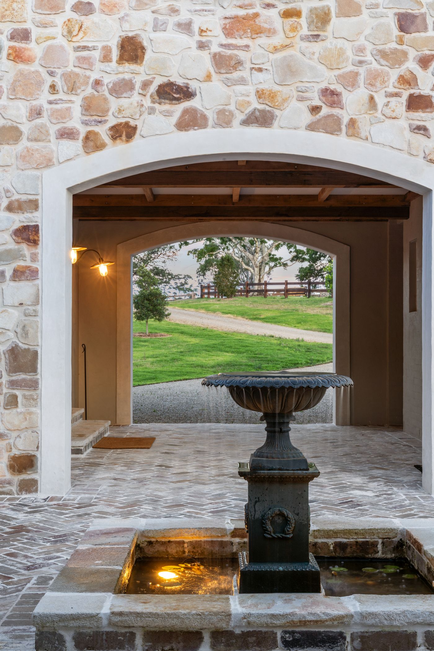 A stone barn entry lit at dusk with a brick courtyard and fountain