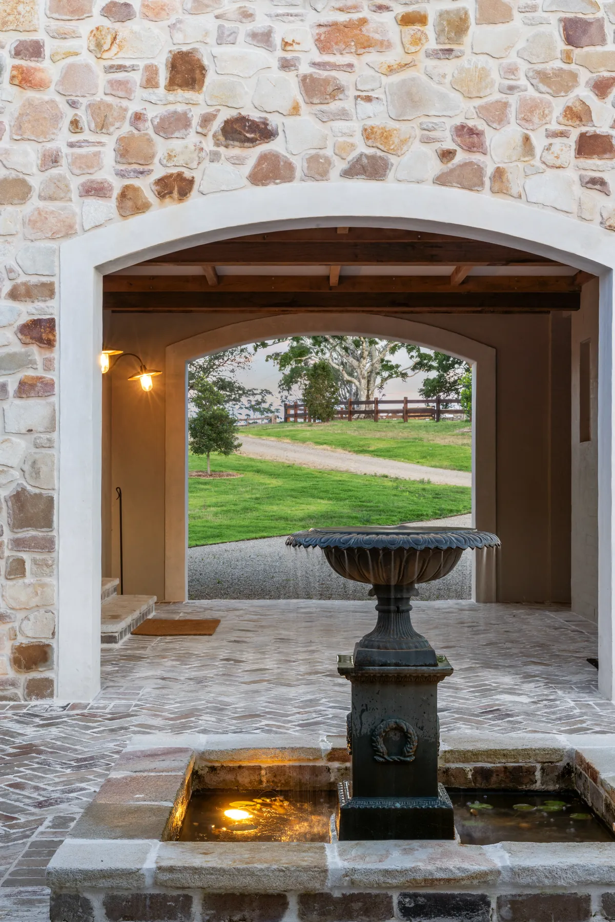 A stone barn entry lit at dusk with a brick courtyard and fountain