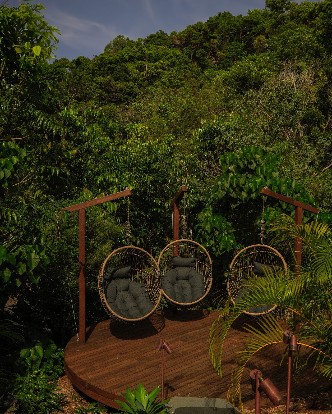 Hanging chairs on a round timber deck above a hillside garden